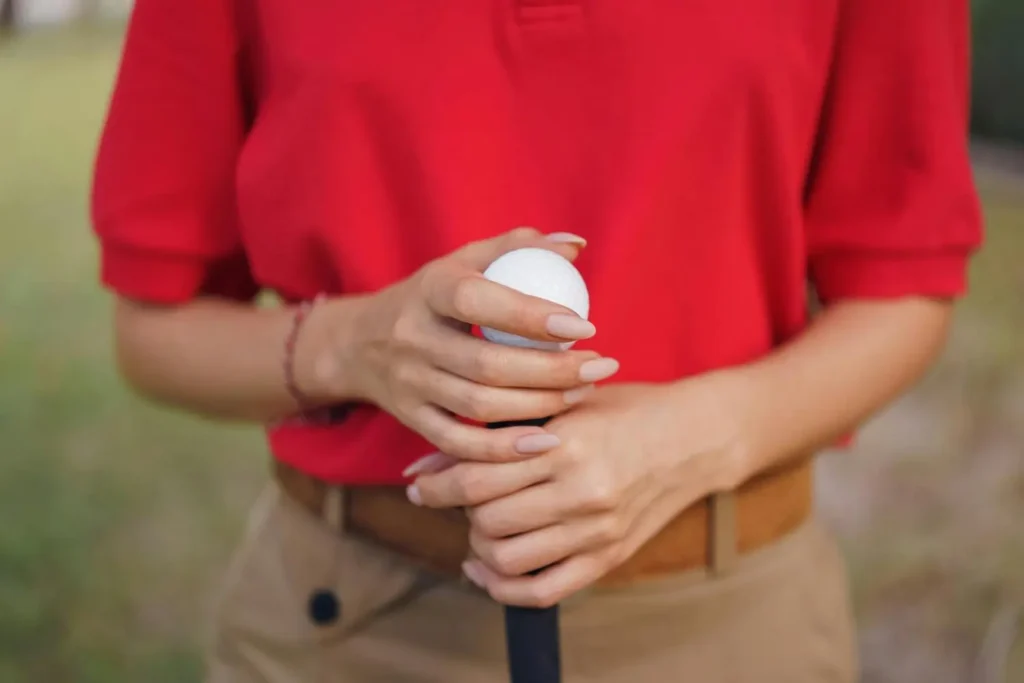 Close-up of a golfer's hands demonstrating a guide for golfers, wearing a red shirt and standing outdoors on a golf course.