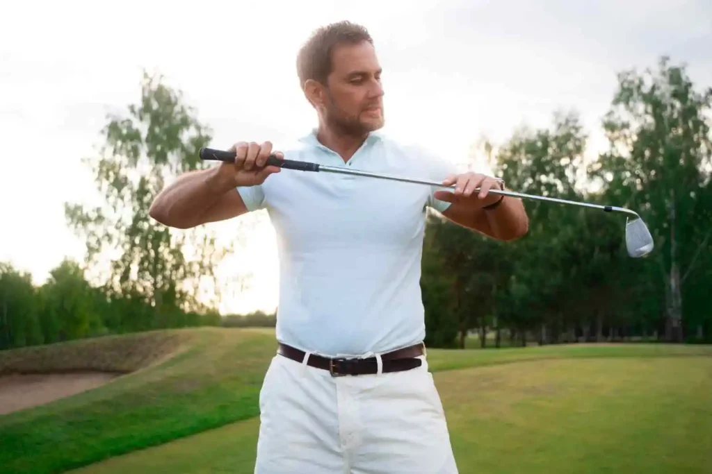 A golfer adjusting his grip on a driver while standing on a golf course, surrounded by lush greenery.