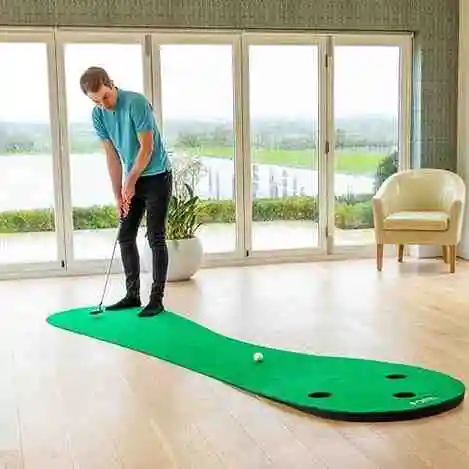 An outdoor putting green designed for indoor and outdoor use, featuring a kidney-shaped artificial turf surface with multiple holes. A golfer practices putting in a bright room with large windows overlooking a scenic view. Ideal for improving putting skills at home.