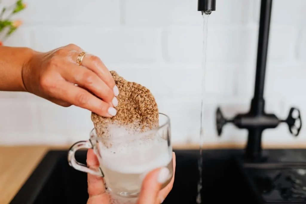 A person washing a glass mug with a sponge, demonstrating a cleaning method that can be applied as a golf grip solvent alternative.