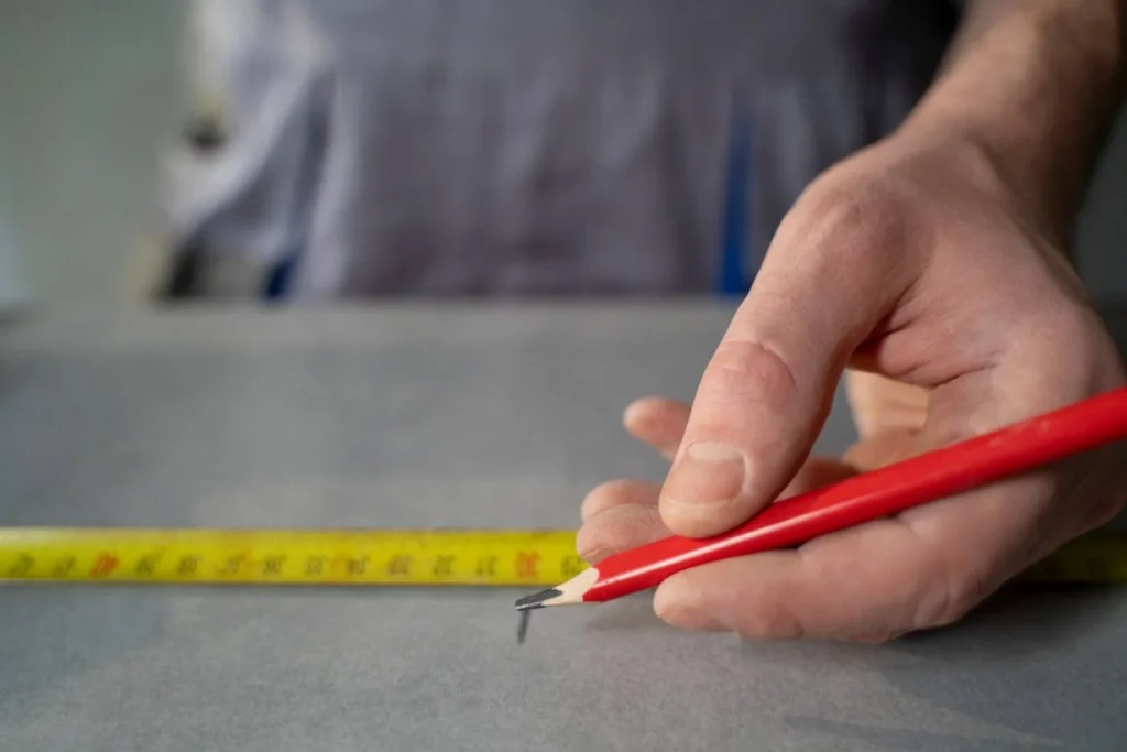 A person marking measurements with a red carpenter's pencil, similar to determining the correct golf grip size.