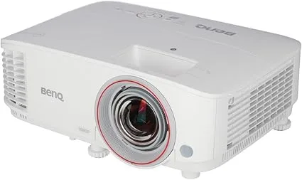 This image shows a white BenQ TH671ST short-throw projector. The projector has a lens with a red ring around it on the front, along with the BenQ logo on the side. There are ventilation grilles on the sides and front of the device.