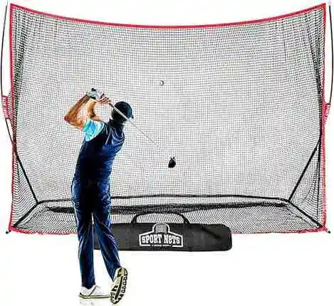 Golfer hitting a shot into a large practice net with red trim and a carry bag placed in front.