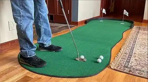 A person is putting on a Big Moss putting green V2 Indoor Putting Green. The green is kidney-shaped with three white flags at the top.
